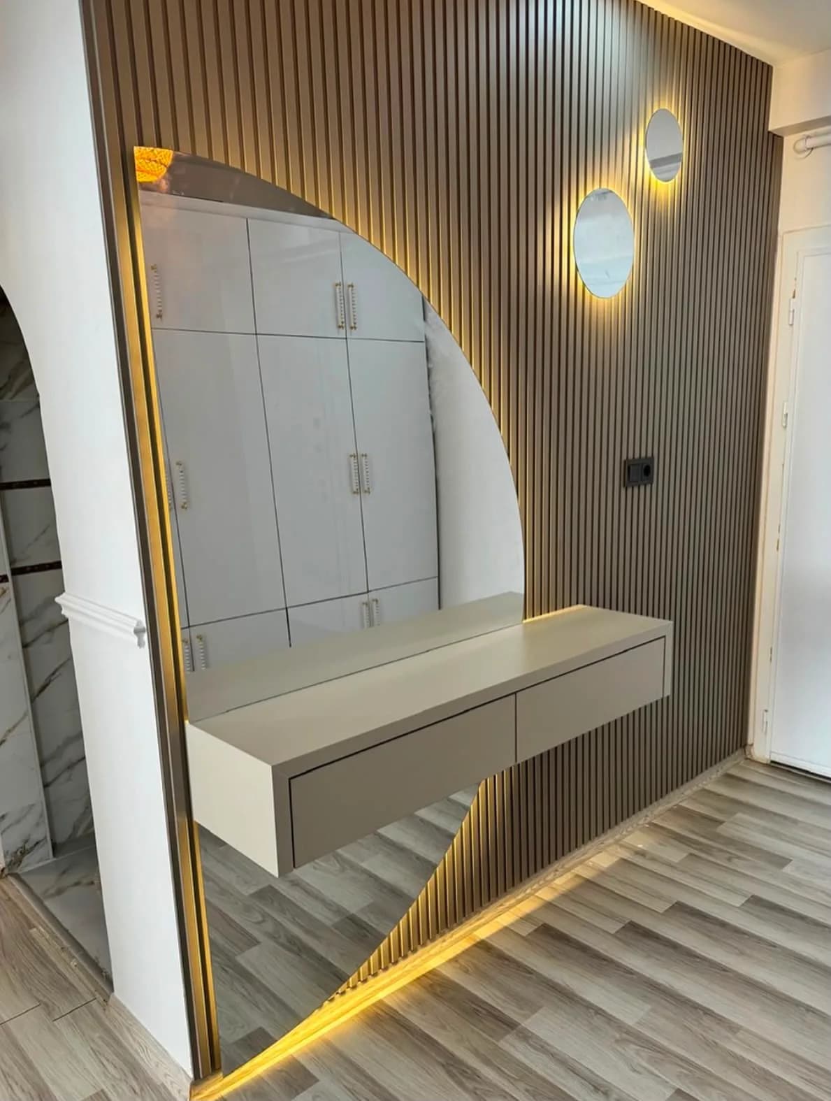 Koyu çıtalı panel üzerinde arkadan LED'li yarım daire ayna ve askıda beyaz dresuar